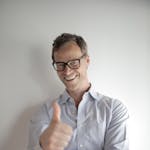 Confident young man in eyeglasses giving a thumbs up gesture, smiling against a white background.
